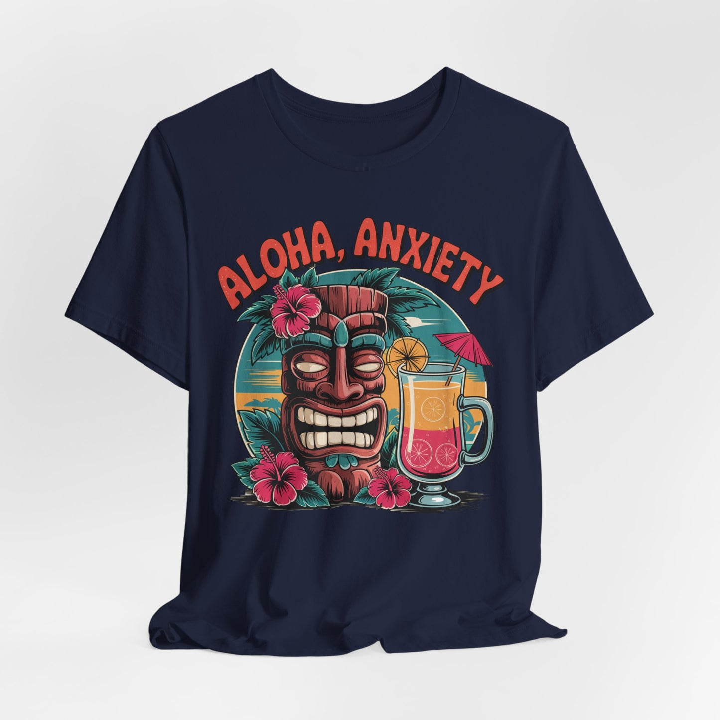 The Aloha Anxiety Unisex Short Sleeve Tiki T-Shirt features a navy blue design with a tiki mask, pink hibiscus flowers, tropical drink with umbrella, and bold red “Aloha Anxiety” lettering on soft Airlume cotton.
