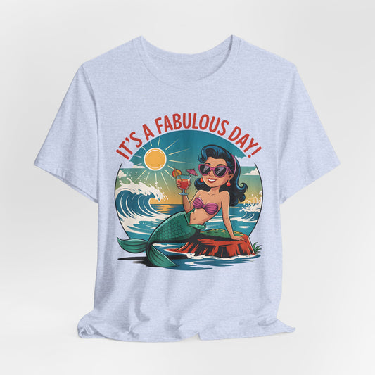 The Fabulous Day Mermaid Unisex Tee is a light gray jersey featuring a cartoon mermaid with dark hair and sunglasses, lounging on a rock by the ocean with ITS A FABULOUS DAY! in bold red text—perfect for fantasy-themed events.