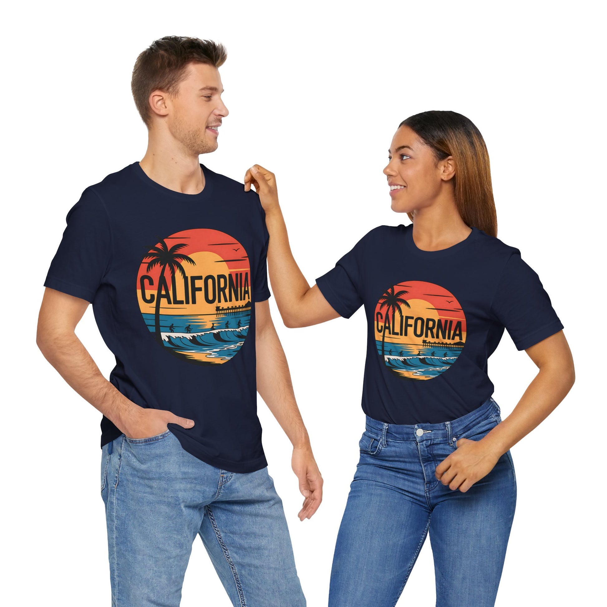 A man and woman smile at each other in matching navy blue California Sunset Graphic T-Shirts, featuring a sunset, palm trees, and ocean design. These breathable cotton tees are perfect for summer and look great paired with blue jeans.