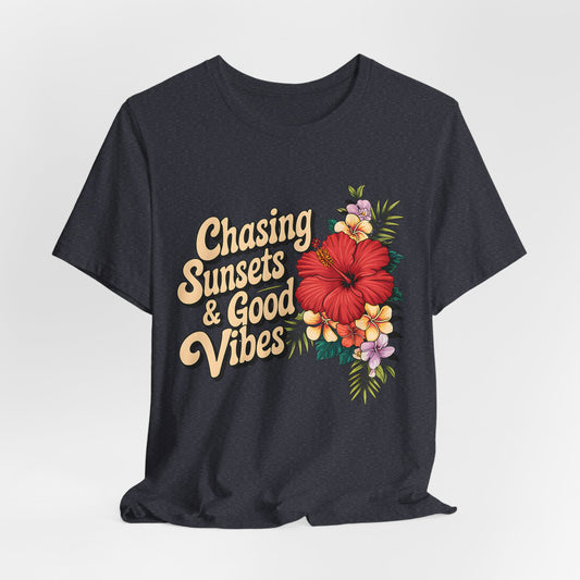 The Chasing Sunsets & Good Vibes Tee is a black unisex jersey shirt for summer adventures, featuring bold floral graphics with a large red hibiscus, colorful small flowers, and green leaves for a carefree vibe.