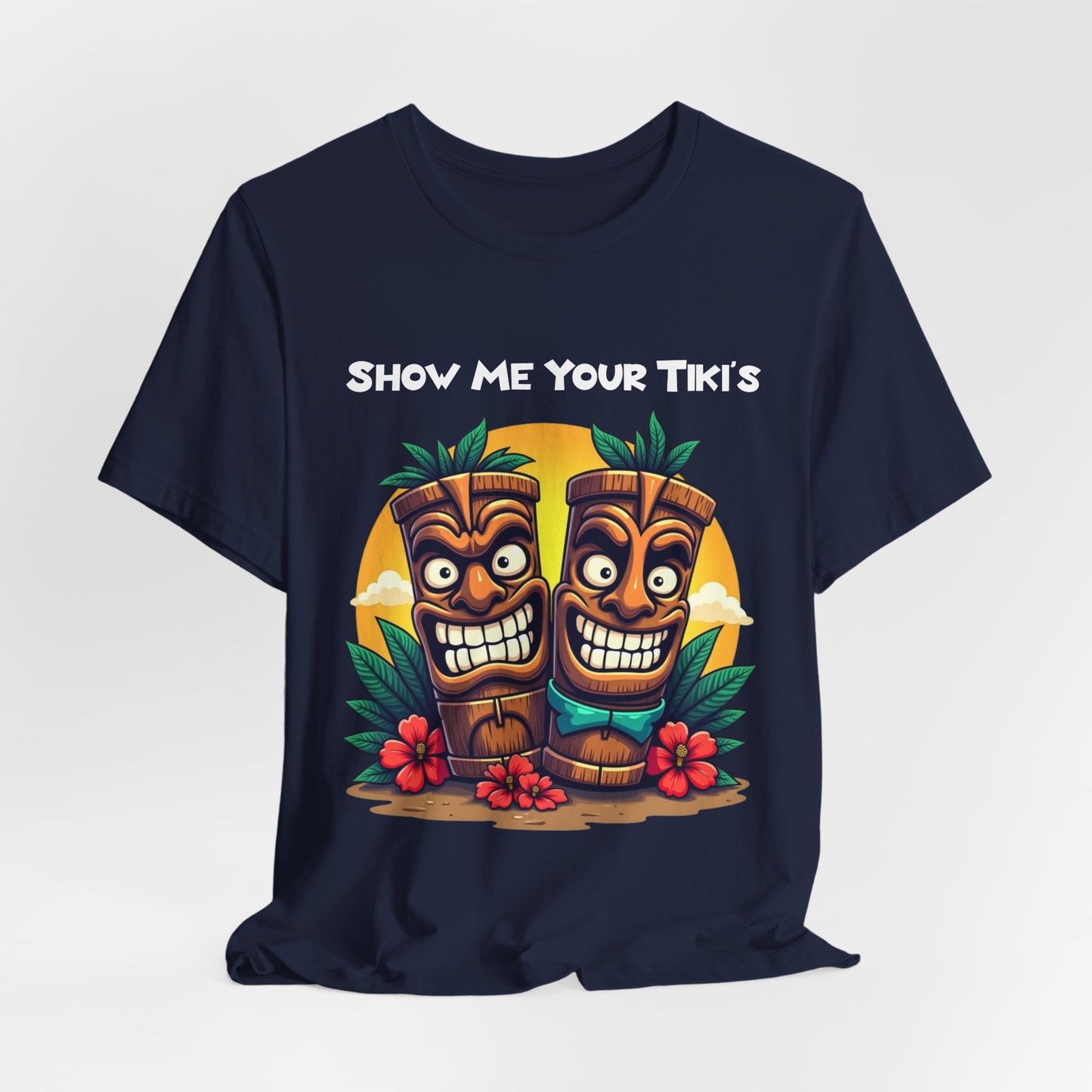 The Tiki Fun Unisex Jersey Short Sleeve Tiki T-Shirt features two smiling tiki statues among tropical leaves and red flowers, “SHOW ME YOUR TIKI’S” in bold white letters, and is crafted from soft Airlume cotton.