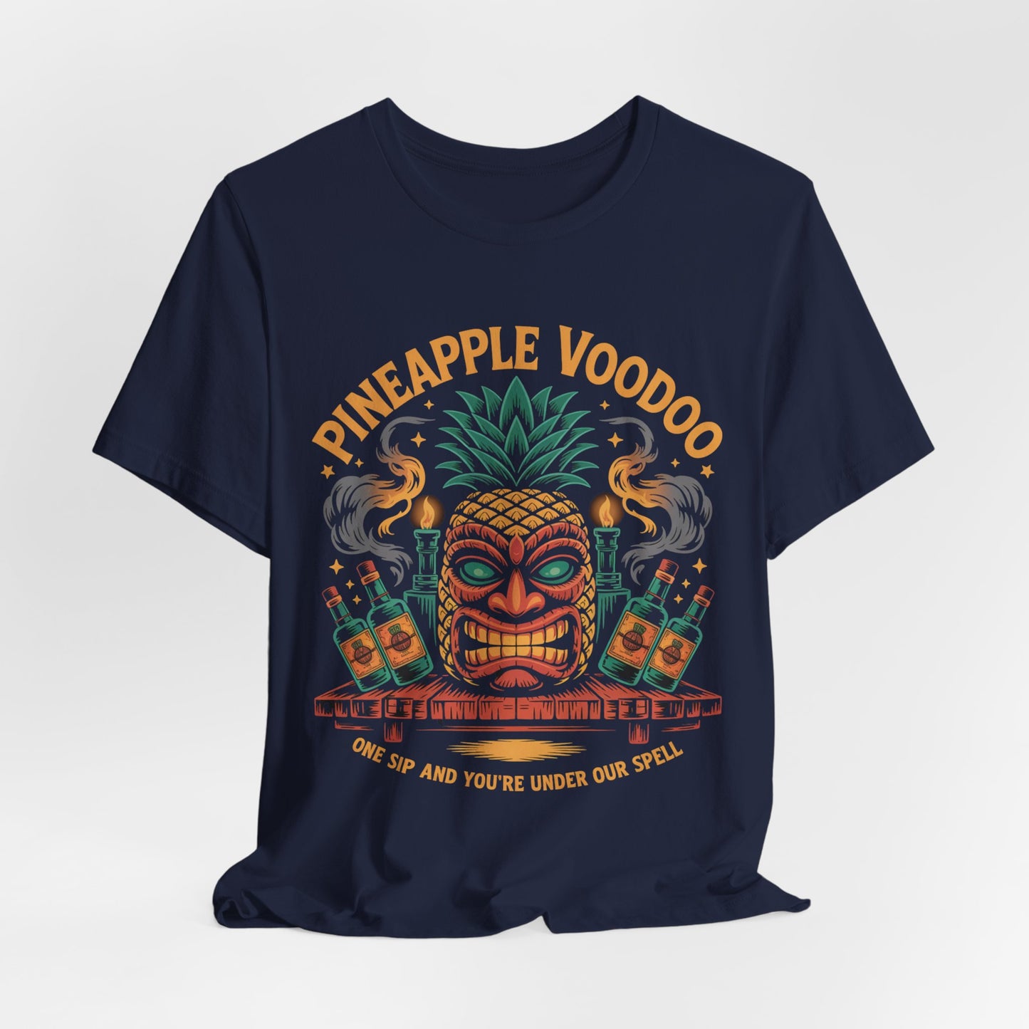 The Pineapple Voodoo Tiki T-Shirt is a navy blue unisex jersey tee with a vibrant tiki mask topped with a pineapple, bottles, smoke, and the words “PINEAPPLE VOODOO” and “One sip and you’re under our spell.”.
