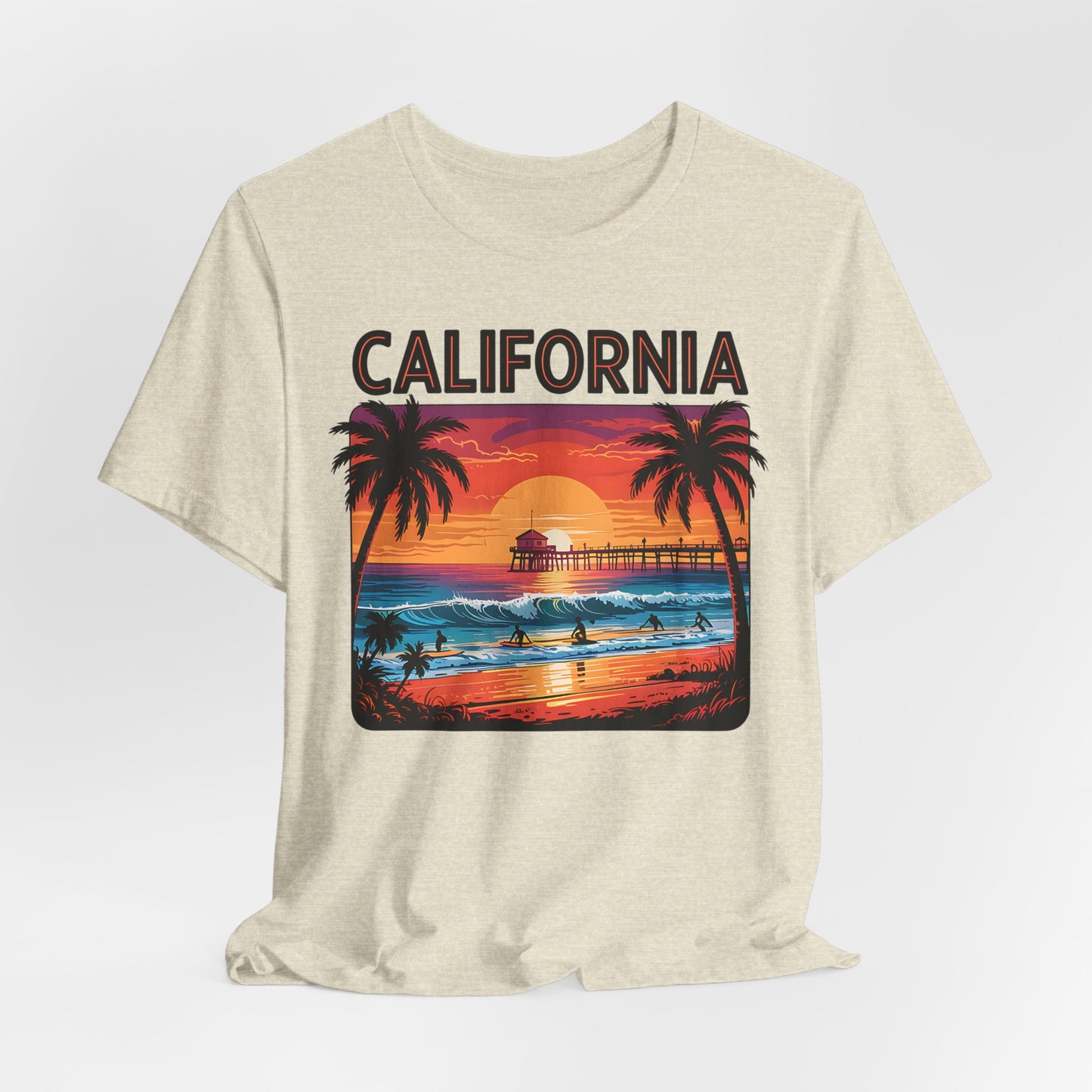 The California Sunset Unisex Jersey T-Shirt - Vintage Beach Vibe features a beige tee with a vibrant beach sunset, palm trees, ocean waves, surfers, a pier, and “CALIFORNIA” printed above—ideal for beach lovers and casual style fans.