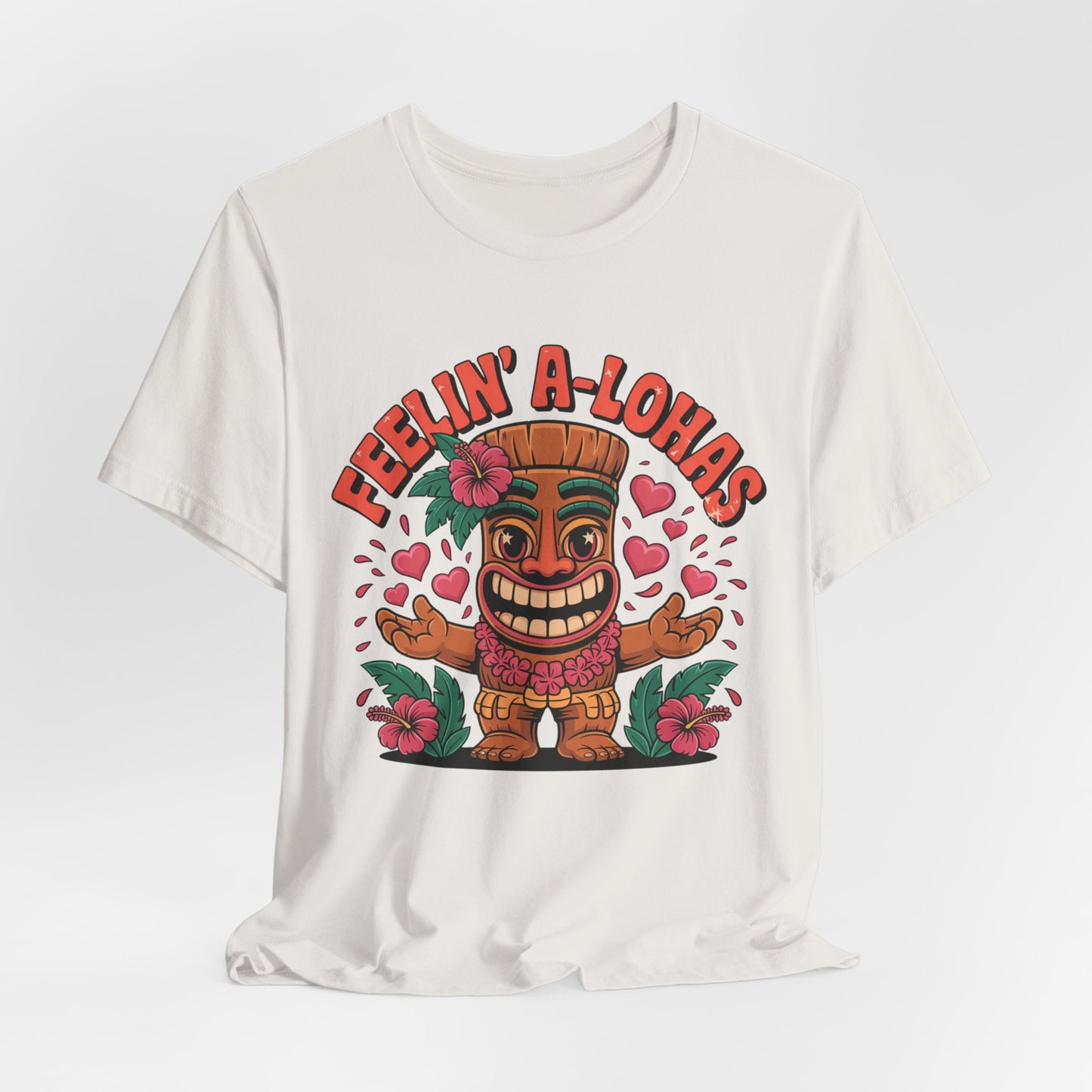 The Feelin A-Lohas Unisex Jersey Tiki T-Shirt features a smiling cartoon tiki with pink hearts and flowers and bold orange “FEELIN’ A-LOHAS” text—a fun tropical graphic shirt perfect for cheerful, casual style.