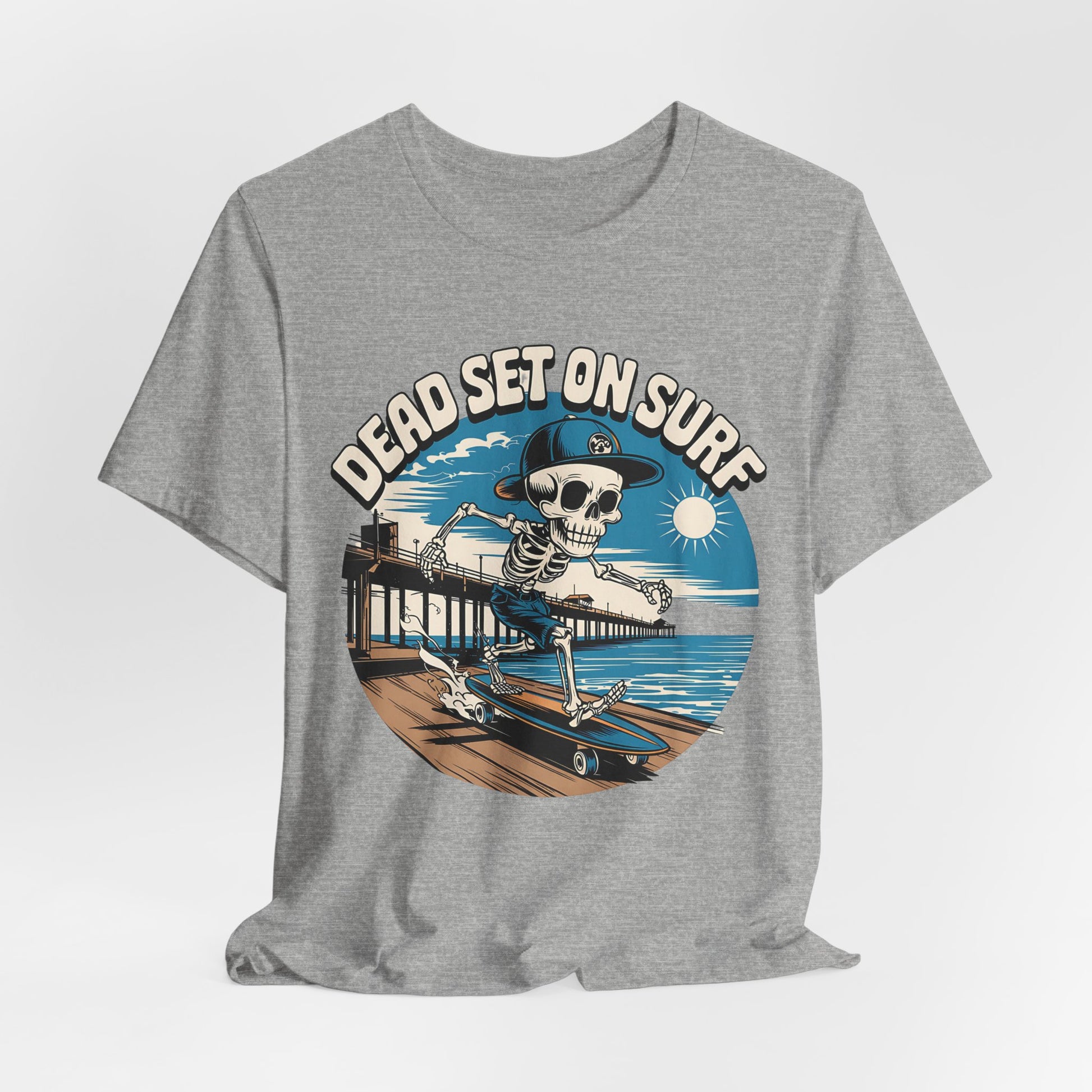 The Skateboard Skeleton Unisex T-Shirt features a cartoon skeleton in a cap skateboarding on an ocean boardwalk with pier, waves, and sun. The surf-inspired design reads DEAD SET ON SURF above the graphic.