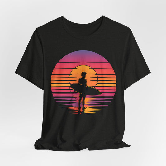 The Retro Surfing Unisex Jersey T-Shirt - Sunset Vibes features a silhouetted surfer with a board against a vibrant sunset, made from soft Airlume combed and ring-spun cotton for all-day comfort and beachy style.