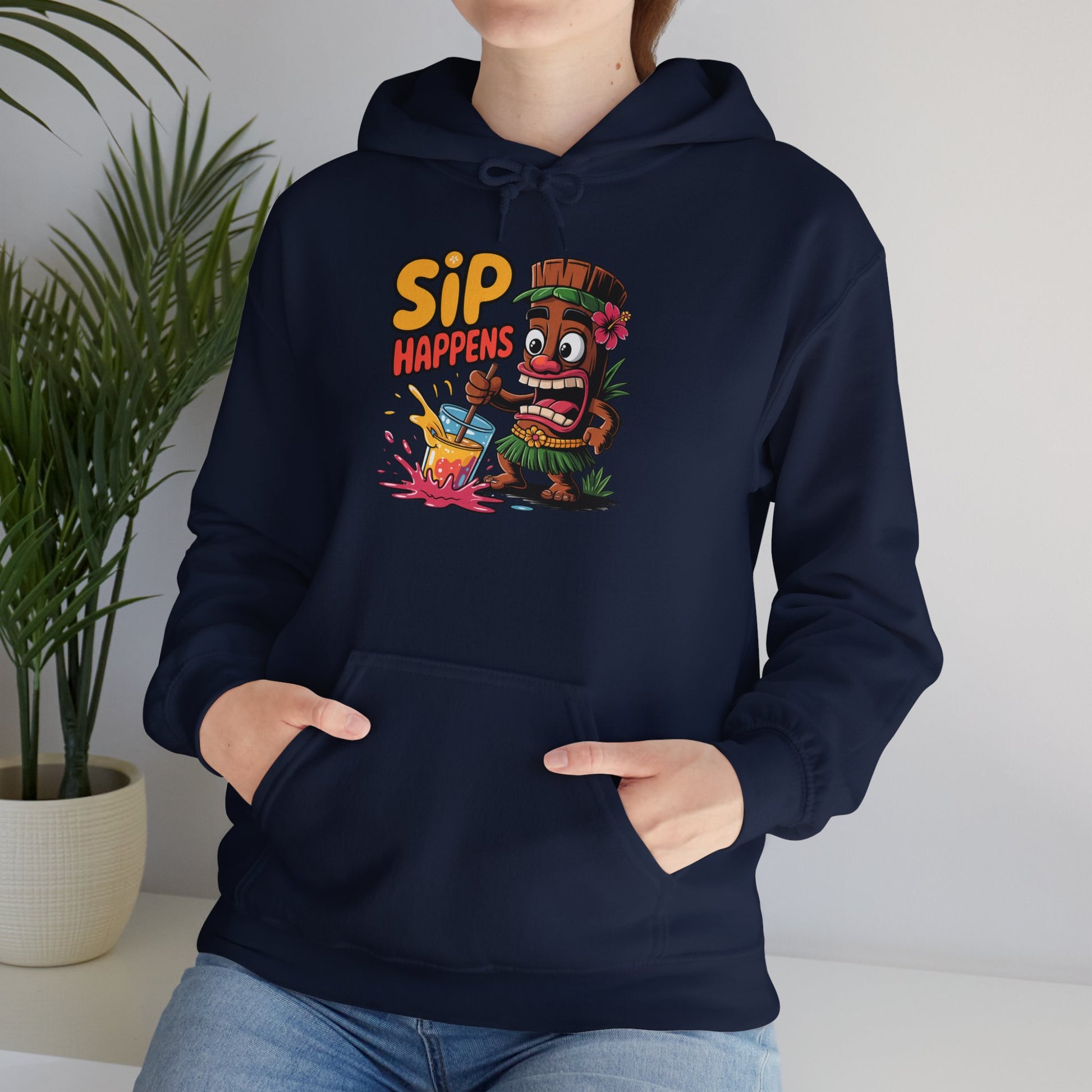 Someone wears the Sip Happens Hooded Sweatshirt—a navy unisex hoodie with a cartoon tiki and playful text—standing indoors by a green potted plant, showing off its fun, relaxed vibes for any casual hangout.