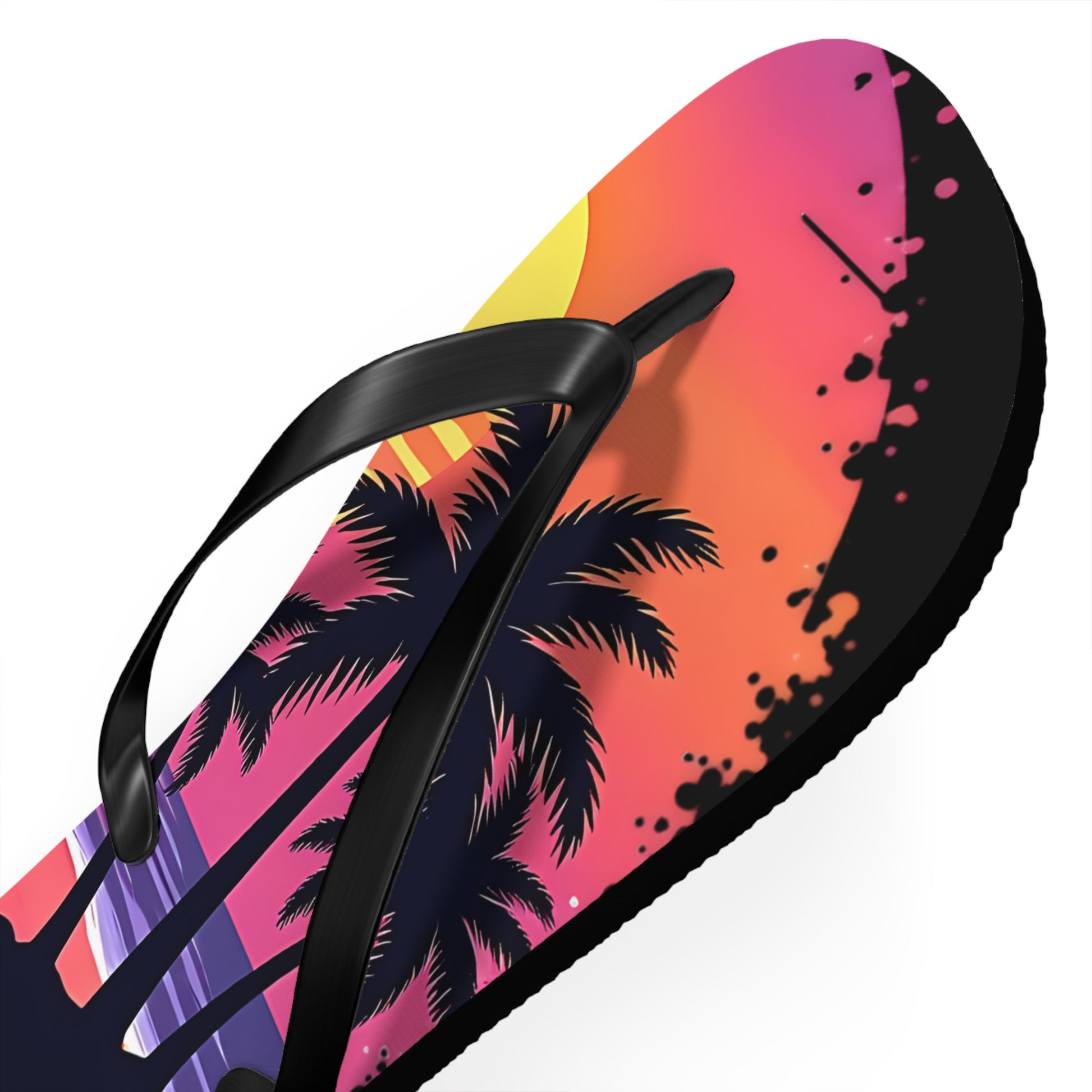 The Tropical Sunset Flip Flops—Beach Vibes Sandals for Summer Fun feature black straps, palm trees, a yellow sun, pink-orange sky, and black paint splatter accents—perfect stylish footwear for your next beach trip.