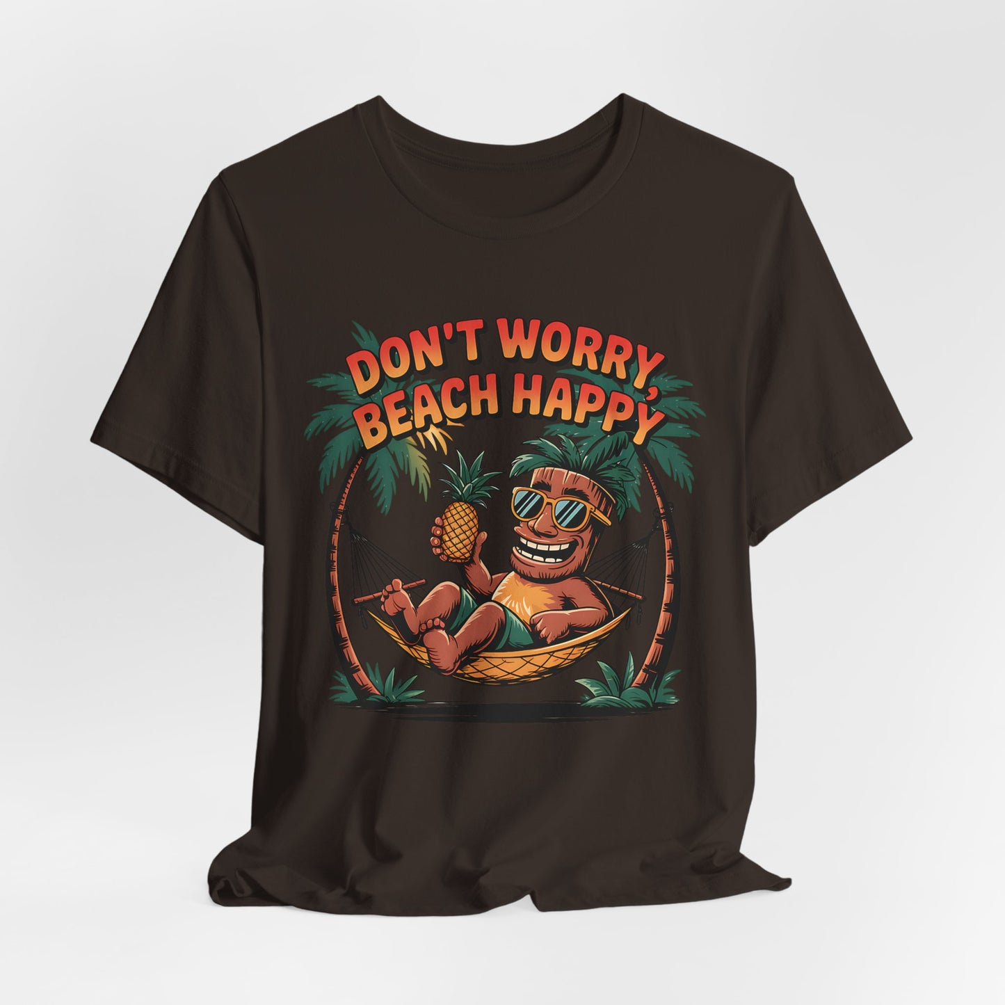The Dont Worry Beach Happy Tiki T-Shirt is a relaxed unisex jersey tee featuring a colorful cartoon in sunglasses lounging in a hammock with a pineapple—ideal for beach lovers and tropical vibes. Text: DONT WORRY BEACH HAPPY.